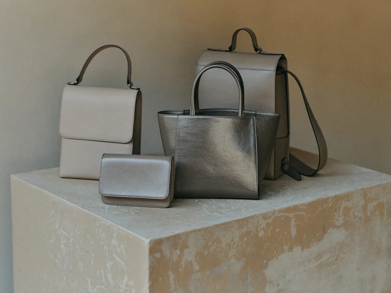 Tote, rucsac și crossbody aranjate pe un soclu de beton, în lumină laterală caldă