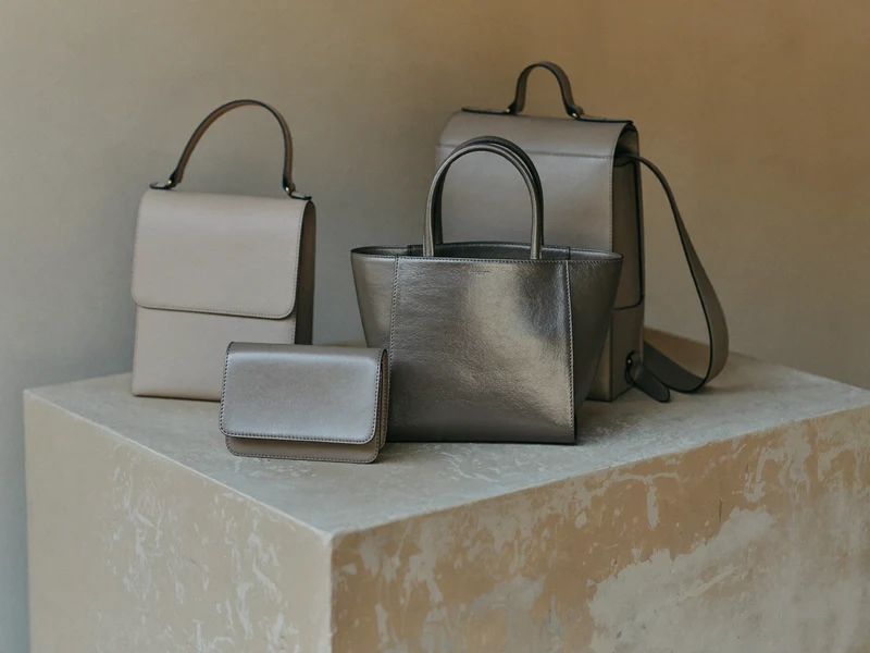 Tote, rucsac și crossbody aranjate pe un soclu de beton, în lumină laterală caldă