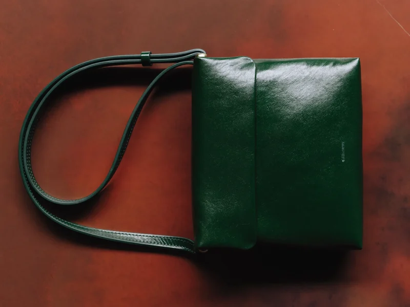 Geantă crossbody din piele verde, cu bretea ușor curbată pe o suprafață teracotă